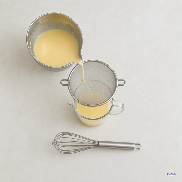 Smooth pale-yellow mango pancake batter pours through a fine-mesh sieve into a spouted measuring jug