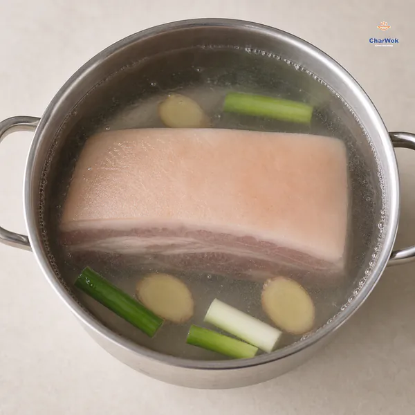 A whole block of skin-on pork belly sits fully submerged in barely trembling water with four scallion segments and three ginger slices
