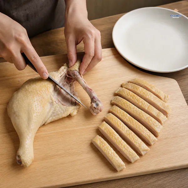 A thin knife follows the bone of a chilled chicken leg beside even skin-on strips arranged about one and a half centimetres wide