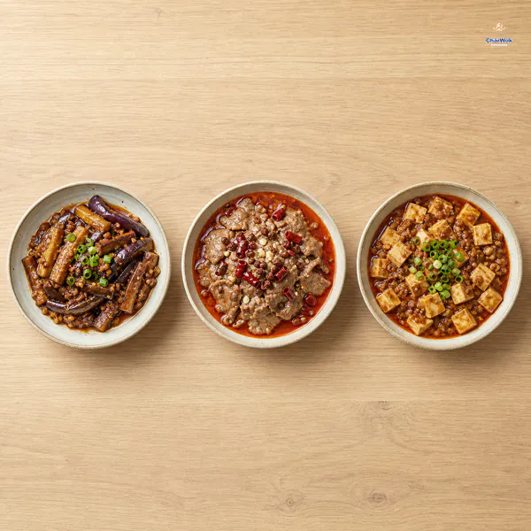 Complete bowls of fish-fragrant eggplant, Sichuan boiled beef and mapo tofu are arranged separately across a pale wooden table