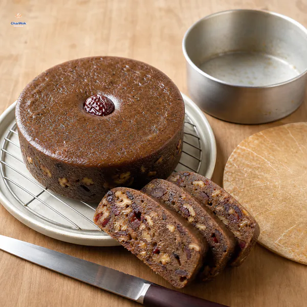 A fully cooled round nian gao stands unmolded beside its empty tin, with three neat slices showing jujube and walnut pieces