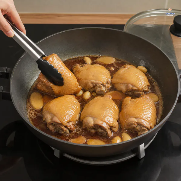 Tongs turn one of exactly six chicken thighs in gently simmering brown braising liquid after the glass lid is lifted