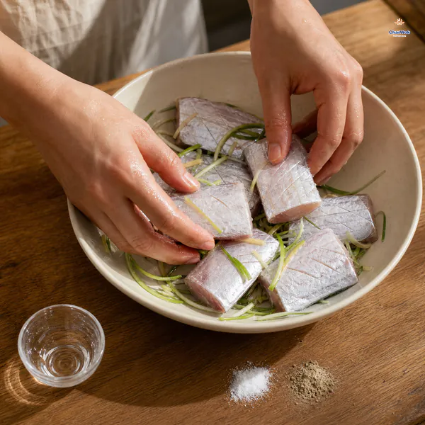 Seven scored belt-fish sections marinate in a shallow bowl with scallion, ginger, Shaoxing wine and a small amount of seasoning liquid