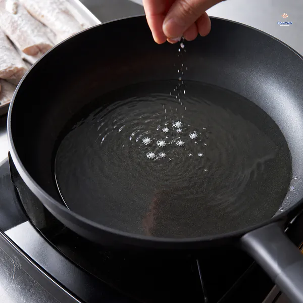 A thin layer of oil shimmers in a dark pan while a pinch of cornstarch forms tiny bubbles at the surface