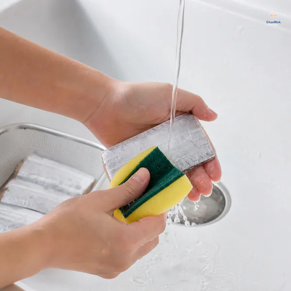 Hands rub the silvery surface of a whole gutted belt fish with a clean green scouring pad under running water