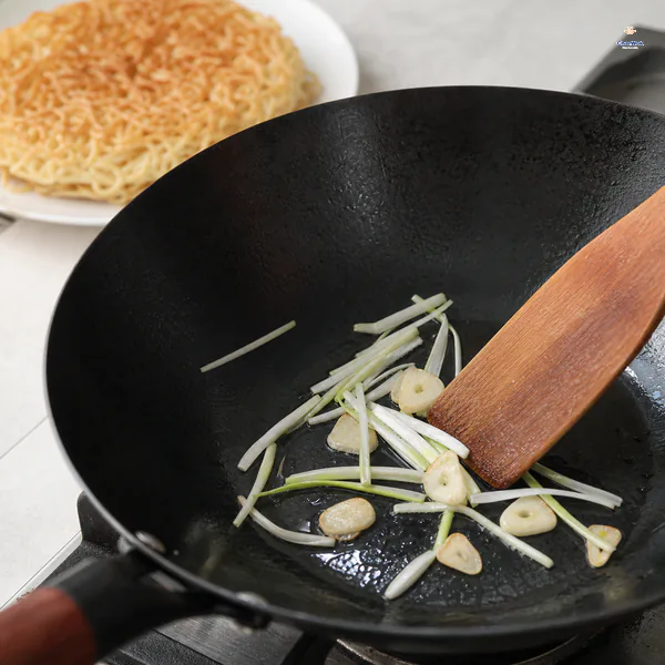 Pale scallion-white slivers and thin garlic slices sizzle briefly in a thin oil film while the crisp noodle cake waits on a plate