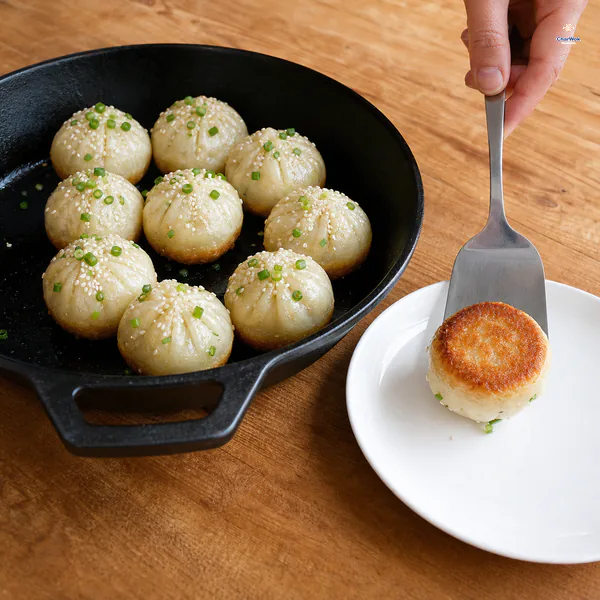 A spatula turns a finished pork bun deep-golden bottom-up onto a white plate beside the dry pan