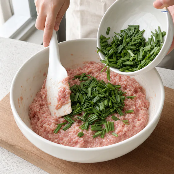 Short flat pieces of Chinese garlic chive are tipped into the finished pork filling beside a silicone spatula
