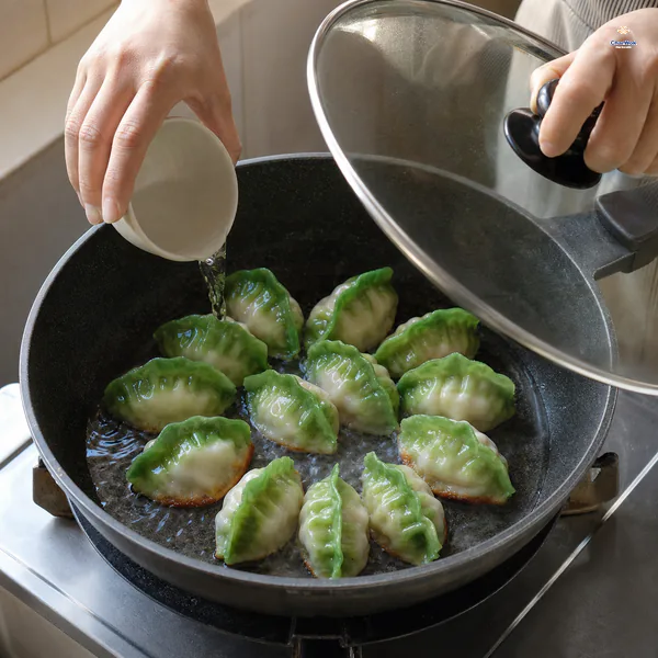 Water is poured to one-third of the dumplings' height as a glass lid lowers over their already golden bottoms