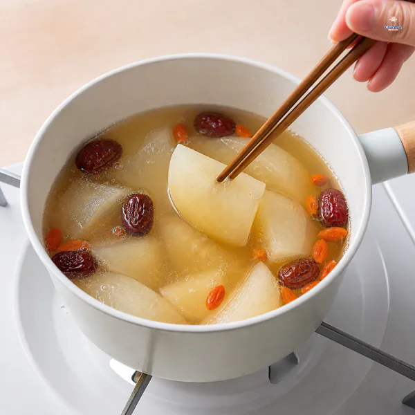 Chopsticks test a translucent tender pear wedge that still holds its shape in clear lightly bubbling broth with red dates and goji berries