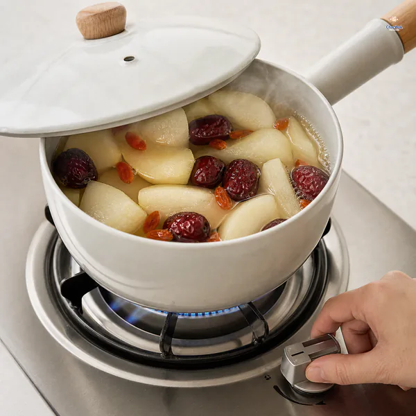 A hand turns the burner down while clear pear broth shows only small edge bubbles and the saucepan lid remains slightly ajar