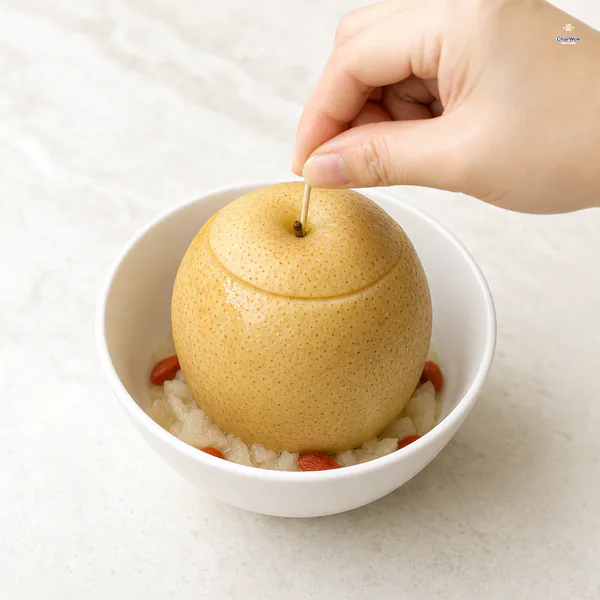One short toothpick secures the replaced lid on a filled Asian pear standing upright in a small heatproof bowl with goji berries and reserved pear flesh below