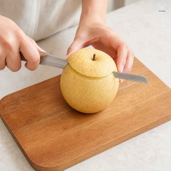 A serrated knife makes one clean horizontal cut through the top quarter of an unpeeled round Asian pear