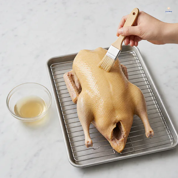 A pastry brush applies a thin even coat of translucent maltose and vinegar glaze to a scalded duck on a rack