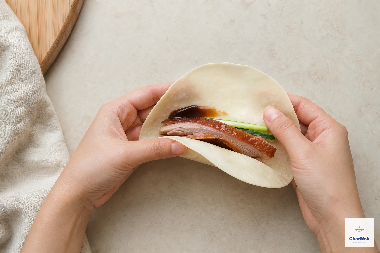 双手把一张柔软春饼包住脆皮烤鸭、黄瓜条、葱丝与少量深色甜面酱