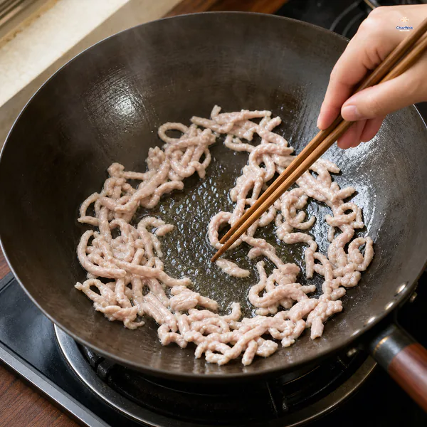 Velveted pork slivers are spread in a loose ring and separated with chopsticks as they turn opaque pale without browning