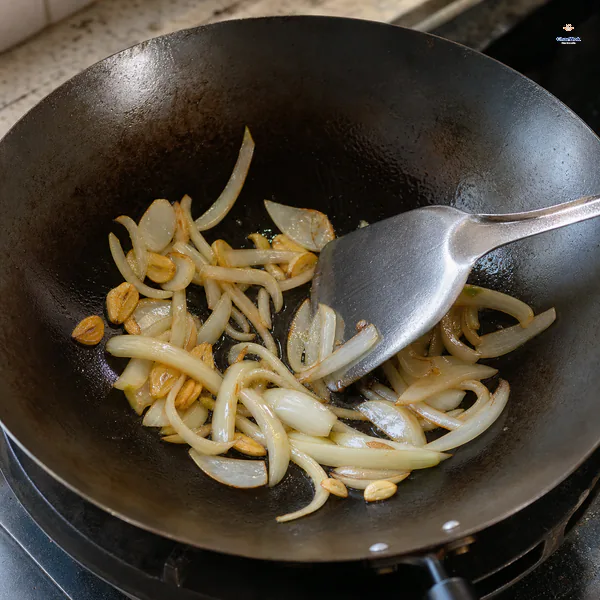 Onion strips soften in a hot wok as thin garlic slices develop pale golden-brown edges