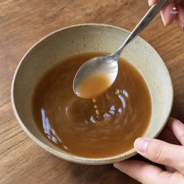 Thin uncooked brown stir-fry sauce is vigorously re-stirred so the cornstarch is suspended and separate drops fall from the spoon