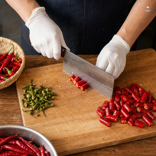 Gloved hands remove dry chili stems and cut the red chilies into rough two-centimetre segments