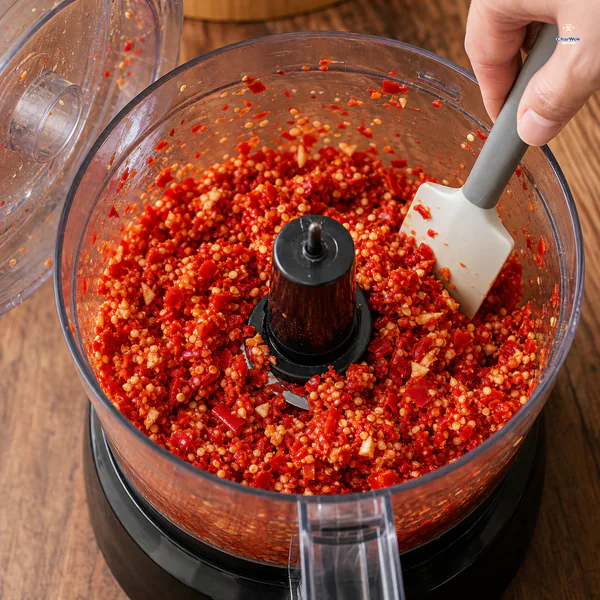 Red chilies with visible seeds are pulse-chopped into a coarse relish in a food processor