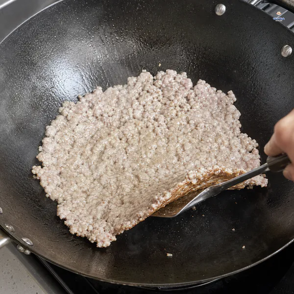 A spatula lifts the lightly browned underside of ground pork spread flat against a hot wok
