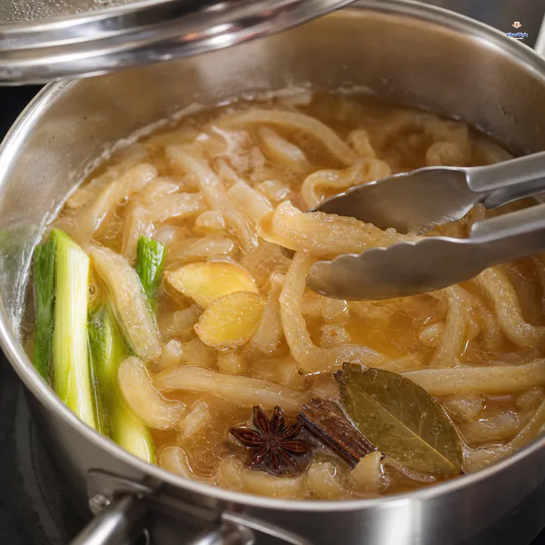Tongs test a very soft pork skin strip in gently bubbling amber broth with scallion, ginger, star anise, cassia and bay leaf