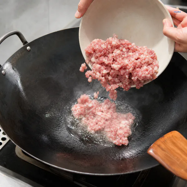 Raw fatty ground pork is tipped into the centre of a smoking-hot carbon-steel wok coated with neutral oil