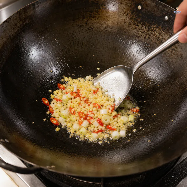 Minced ginger and garlic sizzle with red chili and white scallion parts in a pork-free wok