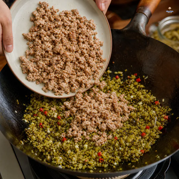 Loose browned ground-pork crumbles are tipped from a plate back onto nearly dry chopped pickled mustard greens