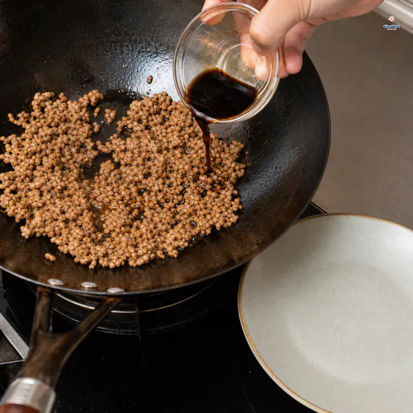 Shaoxing wine and light and dark soy seasoning pours over loose cooked pork crumbles beside an empty plate
