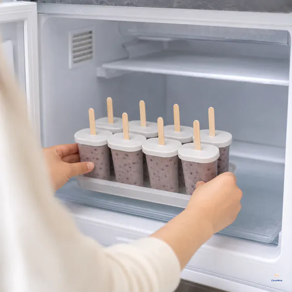A level tray of eight covered red bean popsicle molds with upright wooden sticks is placed on a flat freezer shelf