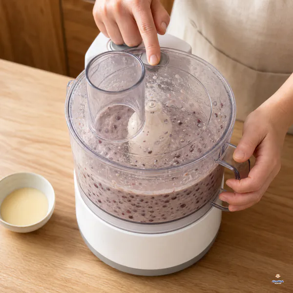 A covered food processor pulses thickened milk with cooked adzuki beans into a pale mauve mixture that still contains many bean flecks