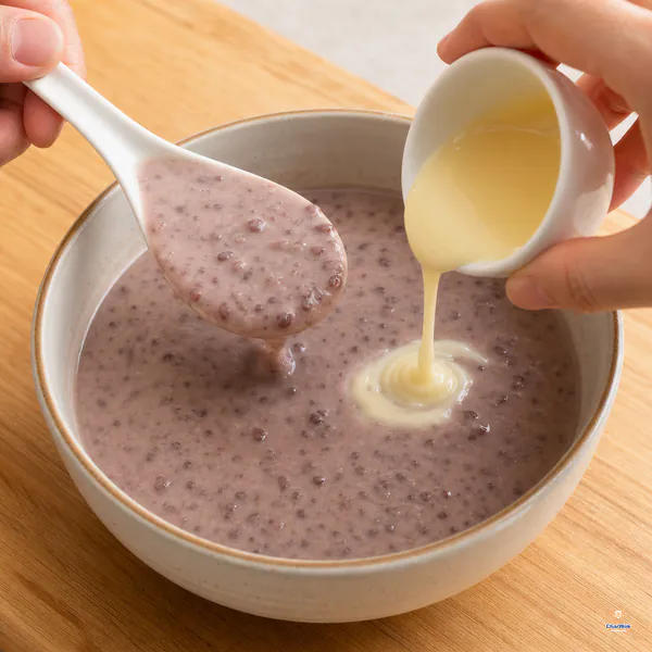 A spoon lifts thick bean-flecked popsicle base while a small ribbon of reserved condensed milk is added to the bowl