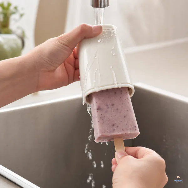 Warm tap water runs only over the outside of an inverted mold as a whole red bean popsicle is pulled out gently by its stick