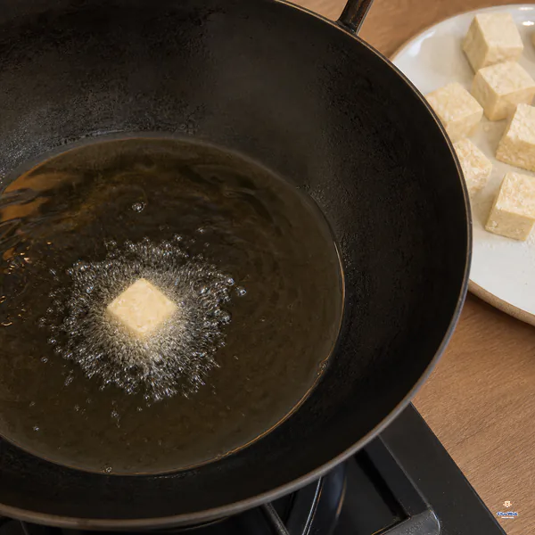One coated tofu cube in a full shallow layer of hot oil is immediately ringed by dense fine bubbles while the rest wait on a plate