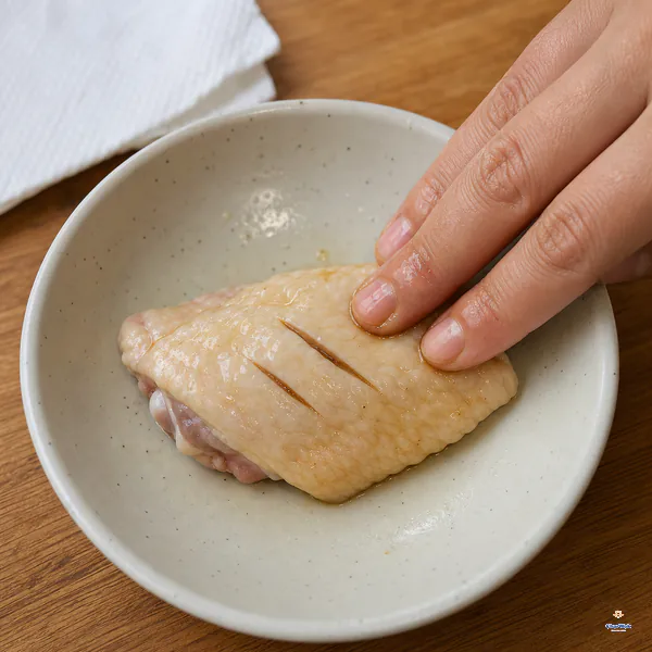 One raw bone-in chicken wing flat has exactly two shallow score marks while light soy sauce and salt are rubbed into its skin