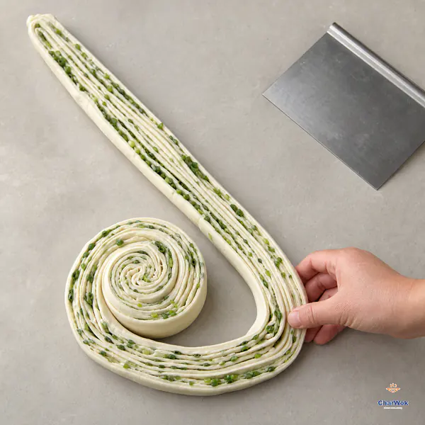 Two lengthwise-cut scallion dough ropes lie cut-side-up while one is guided around a loose spiral coil