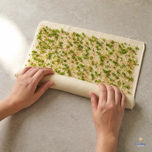 Two hands roll the filled dough from a short edge into one snug cylinder without squeezing out oil