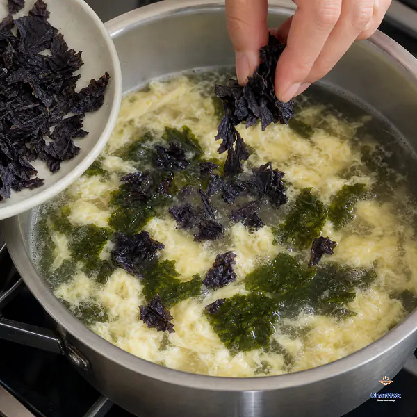 Rough dry Chinese laver pieces fall into clear broth with set egg ribbons while newly hydrated pieces turn soft dark green