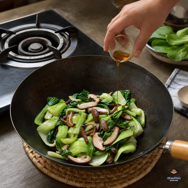 A small stream of amber toasted sesame oil is added to cooked bok choy and mushrooms after the wok has moved to a trivet beside an unlit burner