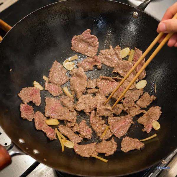 Chopsticks loosen thin beef slices in a hot carbon-steel wok when most surfaces are brown but a few narrow pink streaks remain