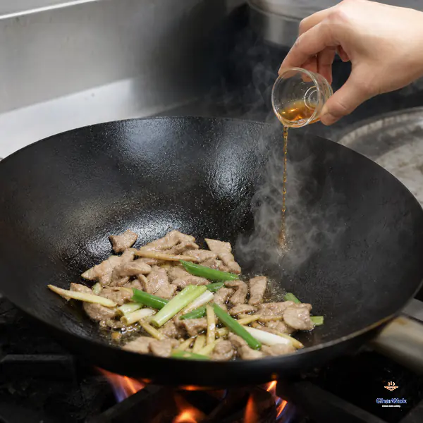 A small stream of amber rice wine hits the bare upper wall of a very hot wok beside sliced pork and aromatics and immediately releases steam