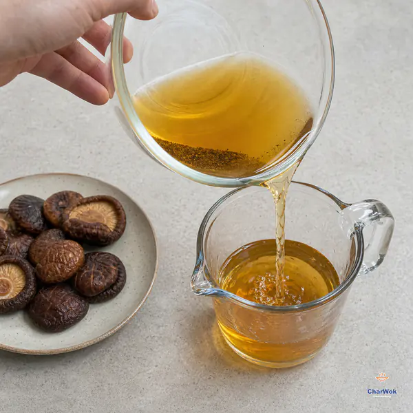 Clear amber shiitake soaking liquid pours into a clean jug while fine dark grit remains at the bottom of the source bowl and plump caps rest separately