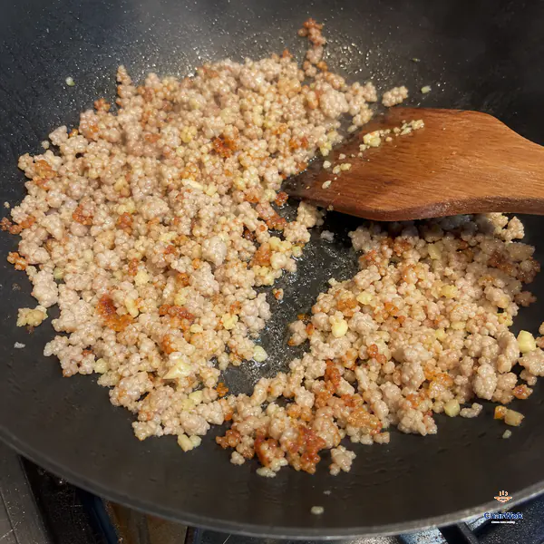 Finely crumbled cooked pork and minced ginger and garlic show many small crisp golden-brown edges in a hot wok with rendered fat