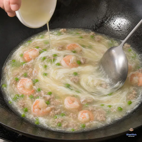 Thinned egg white pours in a very thin stream as a spoon slowly swirls pale glossy shrimp sauce and long silky white ribbons form