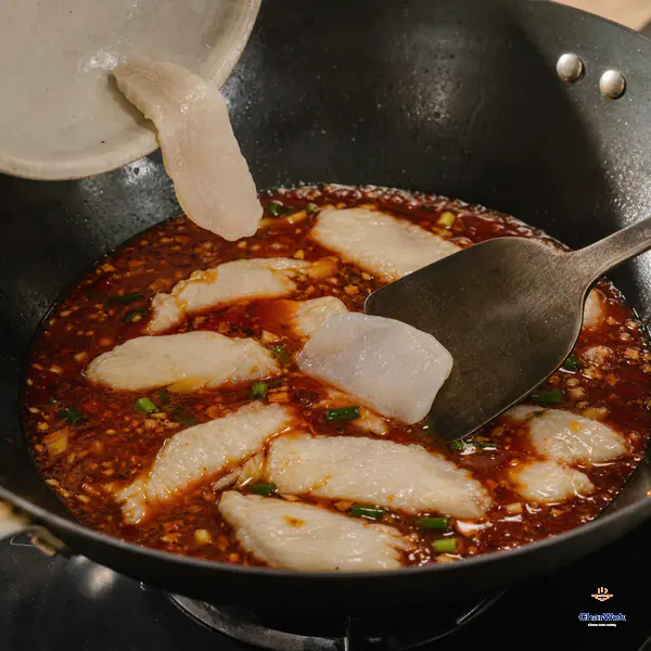 Diagonal white-fish slices enter quiet red broth separately while set slices stay intact and a broad spatula gently nudges one