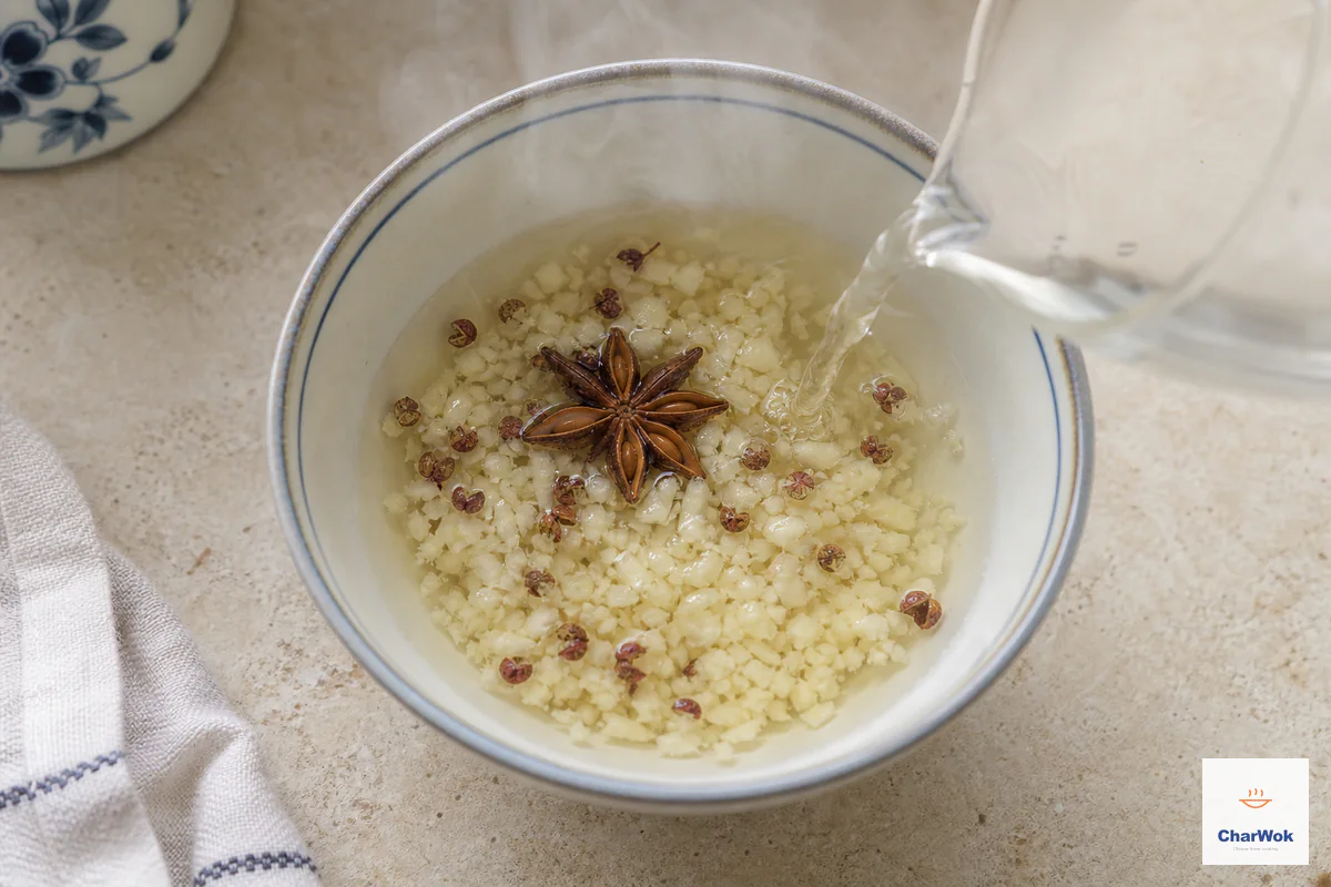 Just-off-the-boil water pours over minced garlic, whole red Sichuan peppercorns and one star anise in a small heatproof bowl