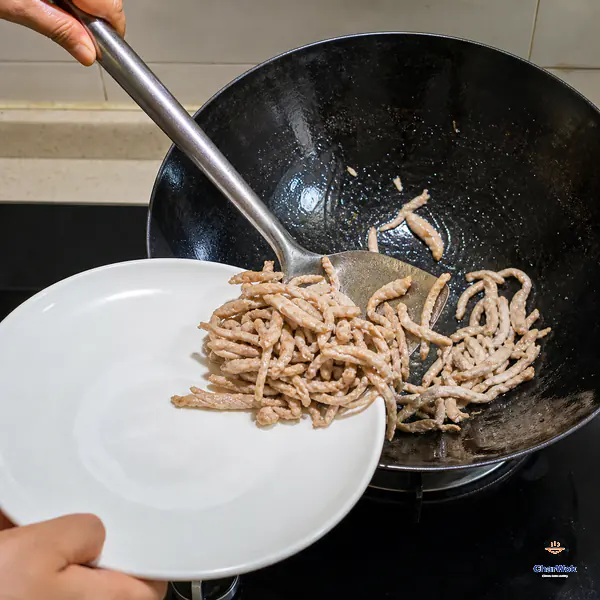Thin pork shreds that have just turned pale are lifted from a hot carbon-steel wok onto a plain white plate
