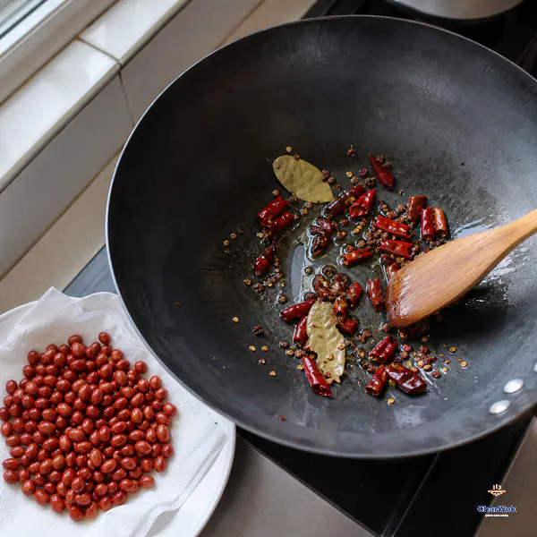Dried chilli, whole Sichuan pepper and bay leaves bloom gently in a thin oil film while fried peanuts drain beside the wok