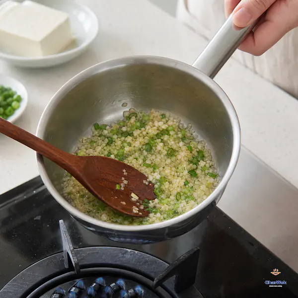 Scallion and minced garlic gently infuse in clear oil as their edges turn pale tea-gold and the small pan leaves the low flame